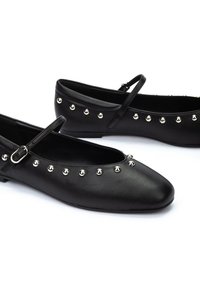 Bailarinas de cuero negro con un acabado suave, que presentan una fila decorativa de tachuelas plateadas a lo largo de la parte superior y una cinta delgada para el soporte.
