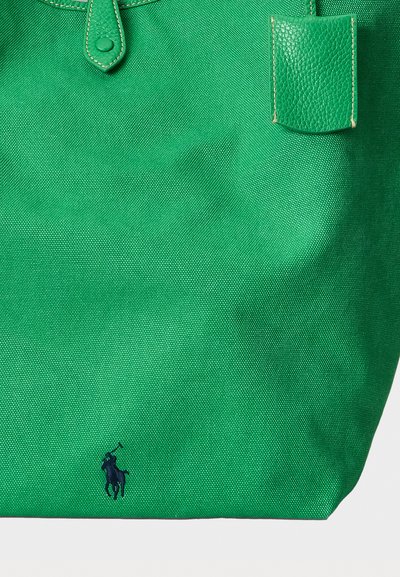 Zaļa teksturēta auduma soma ar ādas siksnām un nelielu tumši zilu polo spēlētāja logotipu apakšējā centrā.