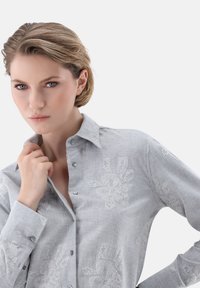 Gray button-up shirt featuring floral white embroidery, lightweight fabric, structured collar, and long sleeves with button cuffs.