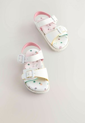 Weiße Sandalen mit zwei verstellbaren Schnallen, rosa Akzenten und einer gemusterten Innensohle, die bunte Früchte und Regenbögen zeigt. Strukturierte Sohle für besseren Halt.