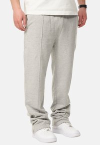 Graue Baumwoll-Sweatpants mit lockerer Passform, ausgestattet mit Seitennähten und elastischen Bündchen, kombiniert mit weißen Sneakern.