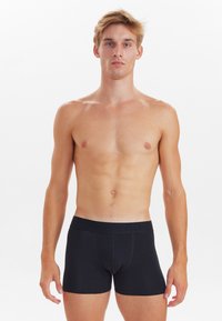 Boxers negros ajustados, confeccionados en una tela suave, con una cinturilla plana con logo en relieve y sin patrones visibles.