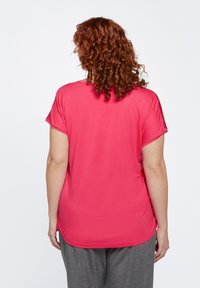 Maglietta a maniche corte con scollo rotondo in tessuto fucsia brillante, caratterizzata da una vestibilità comoda con una texture liscia e un orlo curvato.