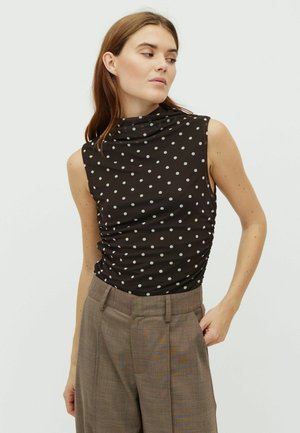 Zwarte mouwloze top met witte polkadots, met een colkraag en geplooide zijkanten, gecombineerd met grijze geruite broek.