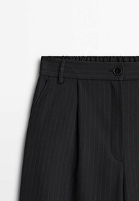 Pantalons noir à rayures avec une ceinture dotée d'une section élastique, une fermeture à bouton et des poches avant. Tissu lisse.