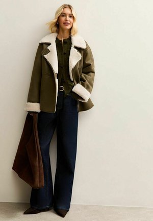 Chaqueta de piel de oveja de color verde oliva forrada de piel de oveja con un cuello amplio, jeans acampanados de color azul oscuro y un bolso de ante marrón. Materiales destacados: cuero, forro de lana.