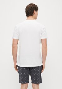 Bela kratka majica s kratkimi rokavi in okroglim izrezom, kombinirana s temno sivimi hlačami z nežnim ponavljajočim vzorcem.