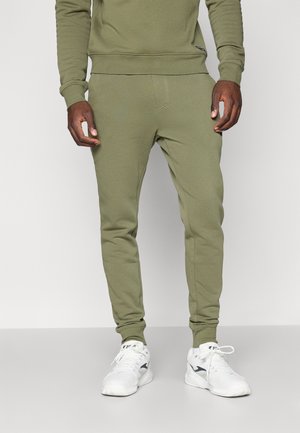 Olive green athletic joggers with a tapered fit, featuring a smooth texture, elastic waistband, and side pockets. Paired with white sneakers.