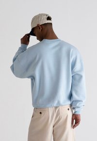 Sudadera de gran tamaño en azul claro con hombros caídos, puños y dobladillo acanalados, combinada con pantalones beige que cuentan con bolsillos laterales.