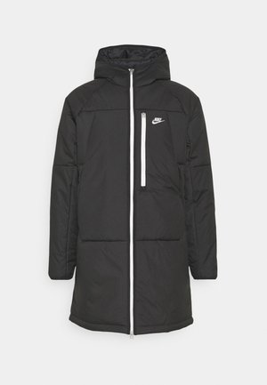 Sort lang polstret jakke med hætte, fuld lynlås foran, brystlomme med hvid lynlås og hvid Nike-logo på venstre bryst.