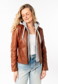 Giacca di pelle marrone con felpa grigia, zip frontale, due tasche laterali e cuciture tono su tono. Indossata con jeans di denim blu chiaro.