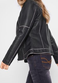 Svart läderjacka med grå sömmar, dragkedja fram, slim fit och sidofickor. Kombinerad med mörka jeans med en böjd fickdesign.