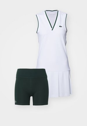 Vestido deportivo sin mangas blanco con ribete verde y falda plisada, combinado con pantalones cortos verdes con una cintura ajustada y acento de logo.
