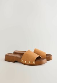 Des sandales à glissière en suède beige avec une large lanière, ornées de clous en ton doré, un talon en bois épais et une semelle incurvée pour le soutien.