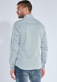 Hemdbluse mit langen Ärmeln in Hellblau mit geometrischem Muster, Knopfverschluss an den Manschetten und strukturiertem Kragen. Getragen mit Jeans.