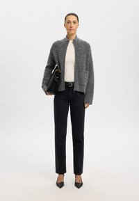 Grå ullkofta med hög krage, två framfickor, tillsammans med en åtsittande krämfärgad topp och svarta högmidjade jeans. Svart läderväska och klackar.