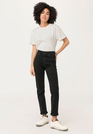 Zwarte high-waisted jeans met een slim fit, gecombineerd met een witte t-shirt met ronde hals. Afgemaakt met opgerolde mouwen en witte sneakers.