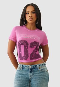 Różowy krótki top z krótkim rękawem z napisem „TRUE RELIGION” i dużą grafiką „02” w ciemnofioletowym kolorze. Gładka tekstura i kontrastowe detale przeszyć.