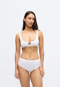 Σετ λευκό μπικίνι με σουτιέν τύπου bralette με φαρδιές τιράντες και εσωτερικό άνοιγμα μπροστά, σε συνδυασμό με σλιπ ψηλόμεσο. Ομαλή υφή και μίνιμαλ σχεδιασμός.