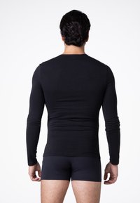 Maglietta nera a maniche lunghe realizzata in tessuto morbido, con scollatura a girocollo e design aderente, abbinata a pantaloni corti neri, vista da dietro.