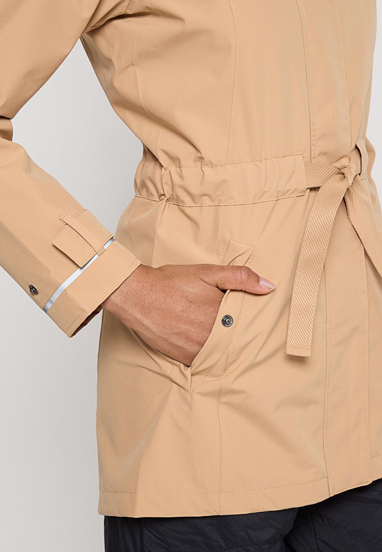 Jasno beżowa kurtka z nadawanym fasonem w talii i kieszeniami; charakteryzuje się gładką powierzchnią i zapięciem na napy; regulowane mankiety z odblaskowymi akcentami.