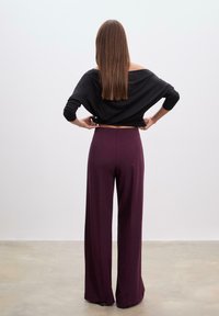Sort off-shoulder top, brede lilla bukser. Glat stof med en afslappet pasform, medium høj talje. Model set fra ryggen, lige hår.