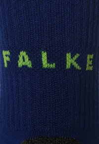 Blauer Socke mit gerippter Textur und grünem "FALKE"-Logo, das in den Stoff eingewebt ist, was die Haltbarkeit und die Markenidentität hervorhebt.