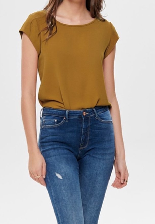 Femme portant un haut manches courtes moutarde rentré dans un jean bleu taille haute avec une petite déchirure sur la cuisse.