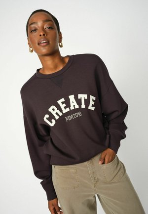 Dark purple sweatshirt featuring large white "CREATE" lettering and "MM2010" underneath. Long sleeves and relaxed fit paired with beige pants.