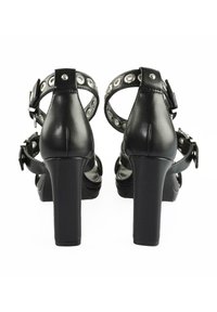 Černé sandály na vysokém podpatku s robustním podpatkem, s členkovým páskem zdobeným kovovými očky a přezkou. Hladký kožený povrch.