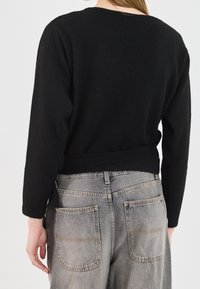 Czarny dzianinowy sweter z zaokrąglonym dekoltem, długimi rękawami i dopasowaną talią, zestawiony z wyblakłymi szarymi, wysokimi jeansami z tylnymi kieszeniami.