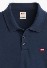 Polo de color azul marino hecho de tela texturizada, que presenta una tapeta de tres botones y un pequeño logo rojo de Levi's en el lado izquierdo del pecho.