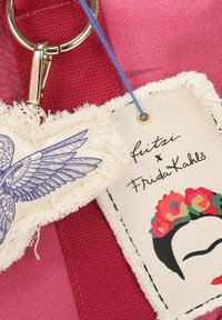 Tela roja con una textura tejida, que presenta dos etiquetas: una con una ilustración de un pájaro de alas azules y otra con la imagen y firma de Frida Kahlo.