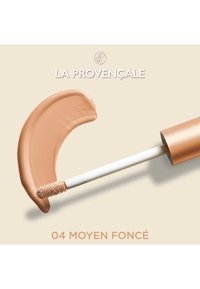 Fond de teint liquide dans un tube avec un capuchon doré ; applicateur en brosse avec des poils doux. La teinte affichée est une crème brun moyen.