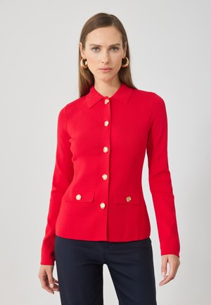 Cardigan tricoté rouge avec col, présentant des boutons dorés et deux poches avant. Coupe ajustée et manches longues. Texture lisse.