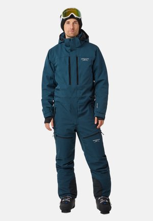 Combinaison de ski bleue avec une fermeture éclair sur le devant, plusieurs poches et des accents noirs. Équipée d'une capuche et en tissu isolant, portée avec des bottes de ski et des lunettes de ski.