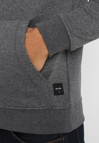 Grijze sweatshirt met een zachte textuur, voorzien van een kangoeroe-zak en geribbelde boorden. Het label aan de onderlinkerkant zegt "ONLY & SONS."