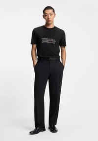 Crna majica od pamuka s grafičkim dizajnom u bijeloj boji i boji, uparena s mat crnim krojenim hlačama i crnim cipelama.