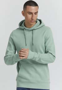 Mintgroene hoodie met een trekkoordcapuchon, geribde manchetten en een voorzak. Heeft een gladde textuur en subtiele branding aan de zoom.