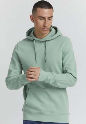 Felpa verde menta con cappuccio regolabile, polsini a costine e tasca frontale. Presenta una superficie liscia e un marchio discreto sull'orlo.
