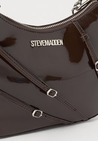 Borsa a tracolla in pelle verniciata marrone con accessori in argento, dotata di chiusura con zip e dettagli a strappo in diagonale. Logo esposto in modo prominente.