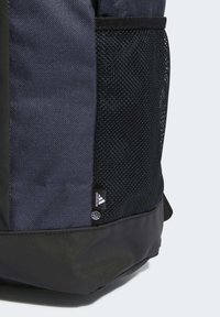 Mochila con un tejido azul marino duradero, bolsillo lateral de malla negra y una base de acento oscura, con una pequeña etiqueta del logo de Adidas en la parte inferior.