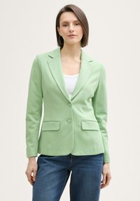 Sacou verde deschis cu rever tăiat, două buzunare frontale și închidere cu un singur nasture, asortat cu blugi albaștri. Textură netedă, ajustat la corp.