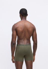 Boxer in verde oliva con elastico nero etichettato "BJÖRN BORG". Tessuto morbido e liscio con una vestibilità aderente e lunghezza fino a metà coscia.