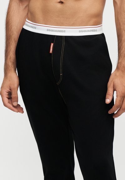 Torso masculin portant un pantalon noir avec une taille élastique blanche avec la marque "DSQUARED2" et une petite étiquette de logo rouge à l'avant.