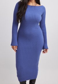 Abito midi a maglia a coste blu, aderente, con maniche lunghe e scollatura a spalle scoperte, indossato con stivali neri.