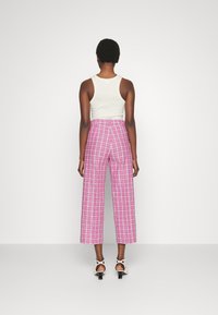 Roze geruite wijde broek met een hoge taille, die een ontspannen pasvorm biedt. Gemaakt van een katoenmix; gecombineerd met een witte tanktop en sandalen.