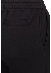 Black sweatpants with a soft texture, featuring an elastic waistband and a small, inset pocket on the rear, highlighting a minimalist design.