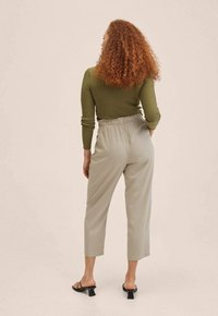 Olijfgroene geribde langemouwen top gecombineerd met lichtgrijze tapered pantalon. De pantalon heeft een elastische tailleband en een enkel-langzaam zoom. Zwarte haksandalen.