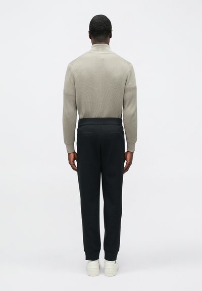 Ανοιχτό γκρι ριγωτό πουλόβερ με ψηλό γιακά, σε συνδυασμό με σκουρόχρωμο παντελόνι στενής γραμμής· το σύνολο χαρακτηρίζεται από καθαρές γραμμές και μινιμαλιστικό σχέδιο.